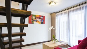 A modern living room with a wooden staircase, a red sofa, a wooden coffee table, a potted orchid, and a colorful abstract painting on the wall. - Legian Village Residence (Legian)