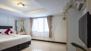 A modern hotel room with a large bed, a flat-screen TV, a mirror, and a window with curtains. - Legian Village Residence (Legian)
