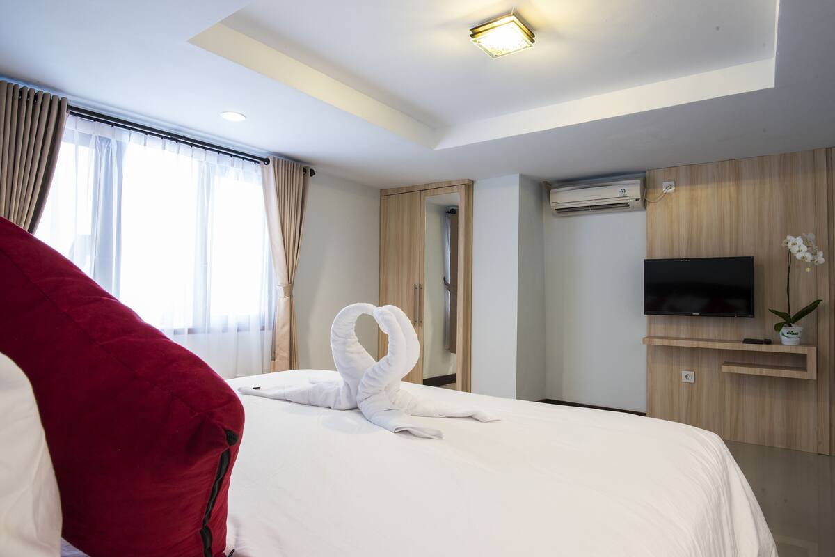 A hotel room with a neatly made bed, a television on the wall, and a mirror.