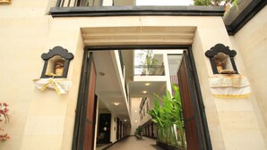 A corridor with a wooden door leading to a room. There are potted plants along the walls and a ceiling light. - Legian Village Residence (Legian)
