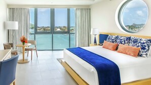 Une chambre d’hôtel avec un grand lit, un miroir rond, une vue sur la mer, un coin repas et une vue sur la ville.
