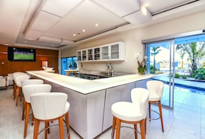 A modern kitchen with a central island, bar stools, and a large window overlooking a pool.