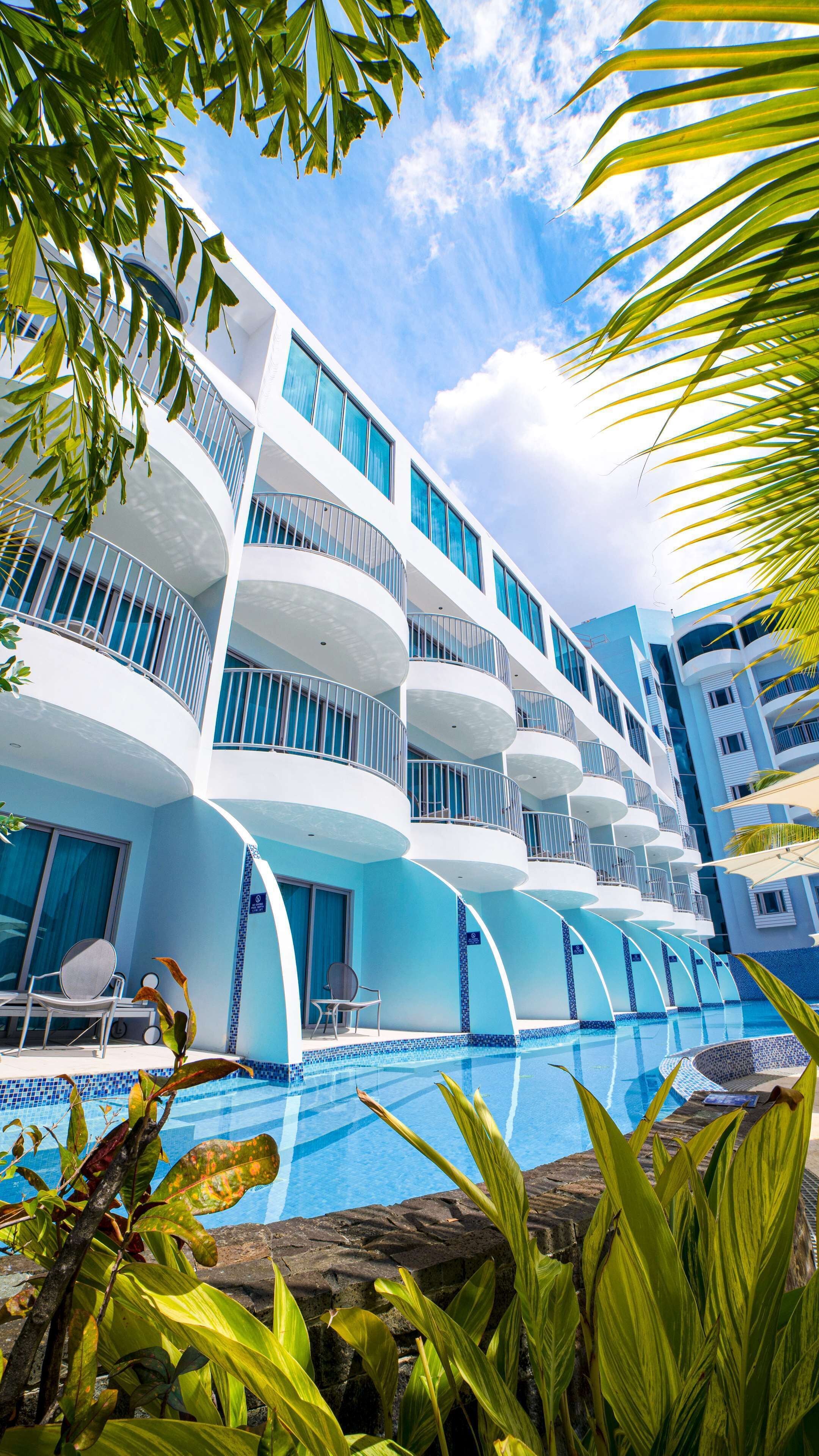 Un hôtel moderne doté de nombreux balcons, d’une piscine et de plantes tropicales.
