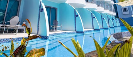 Un hotel moderno con varios balcones, piscina y plantas tropicales.