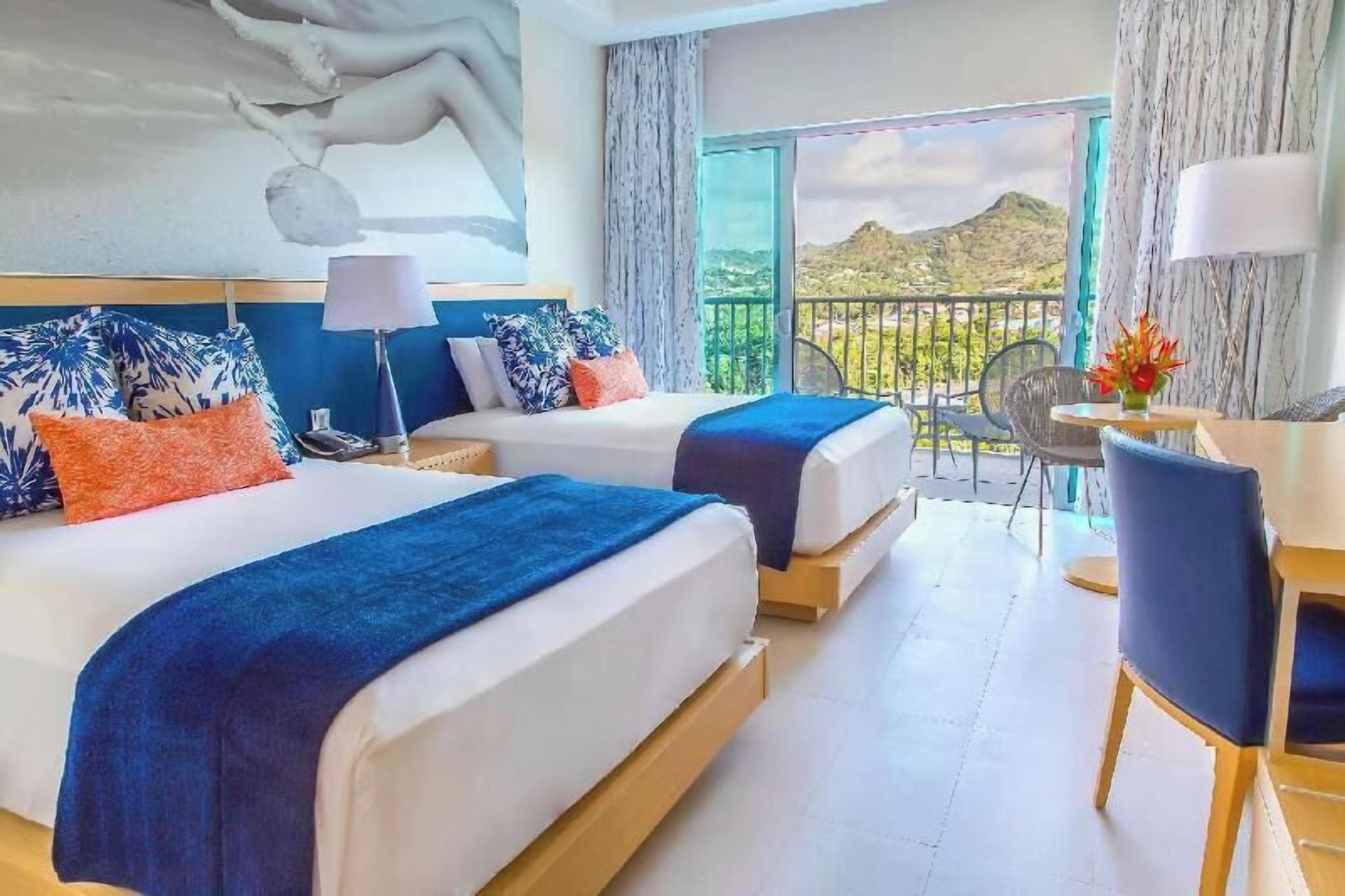 A hotel room with two beds, a balcony, a dining area, and a view of the landscape.