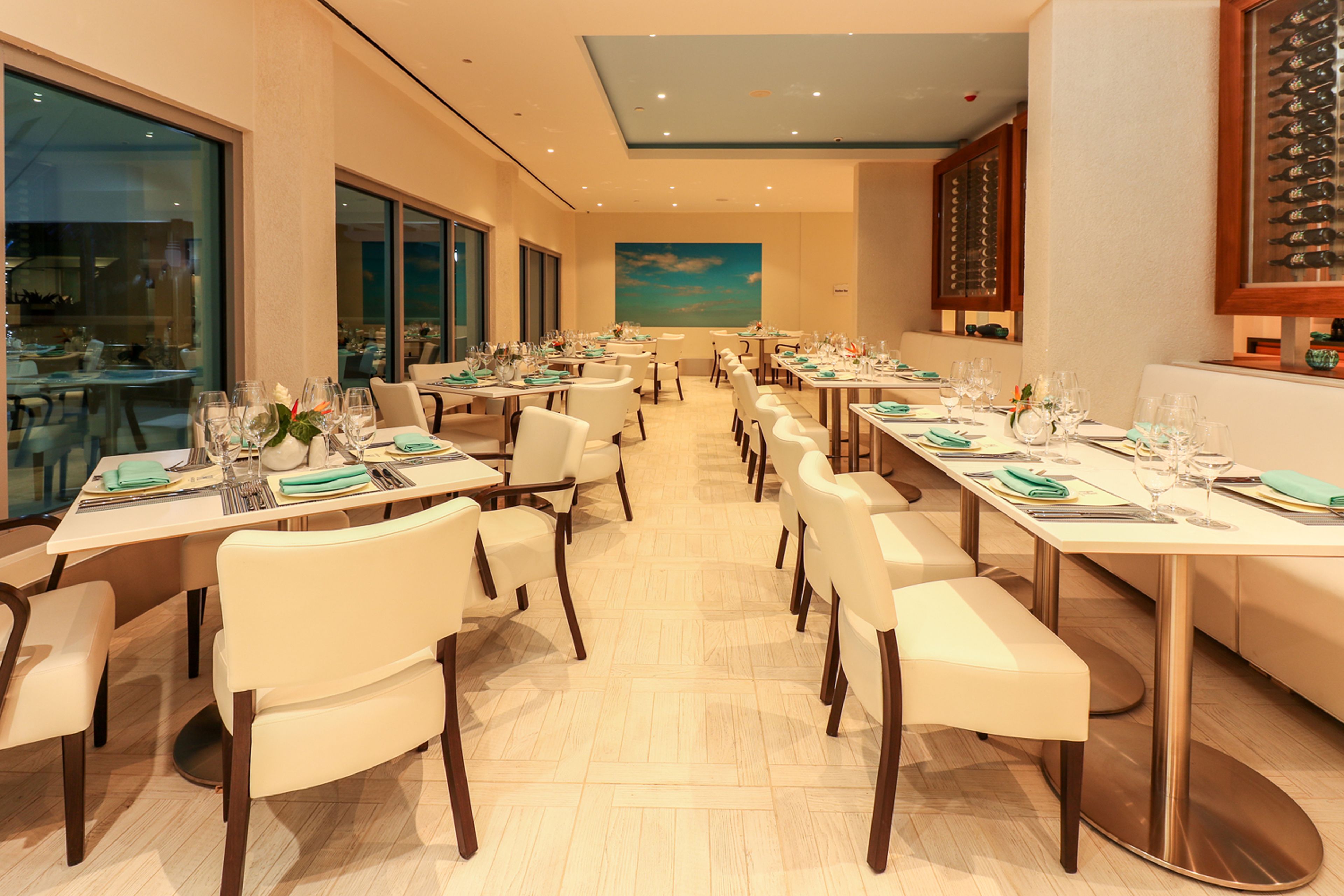 A restaurant with multiple tables set for dining, featuring a view of the sky through large windows.