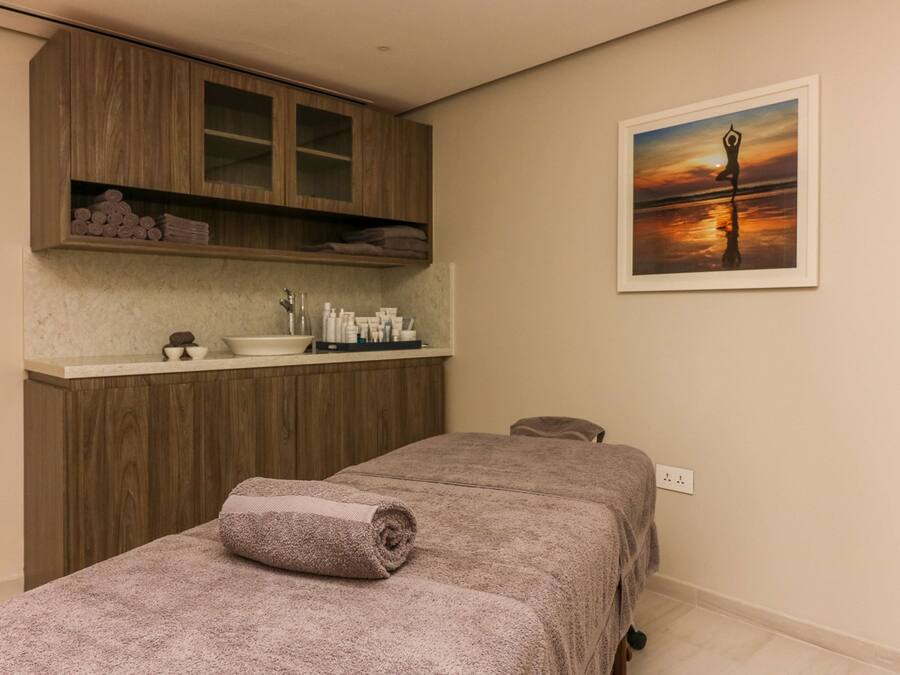 A spa room with a massage table, wooden cabinets, a sink, and a framed sunset painting.