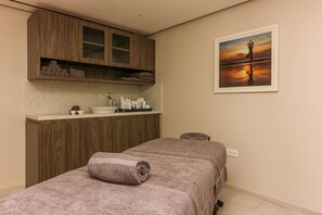 A spa room with a massage table, wooden cabinets, a sink, and a framed sunset painting.