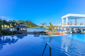 A resort pool area with a clear view of the sea, lounge chairs, and a covered seating area. - Harbor Club St. Lucia, Curio Collection by Hilton (Gros Islet)