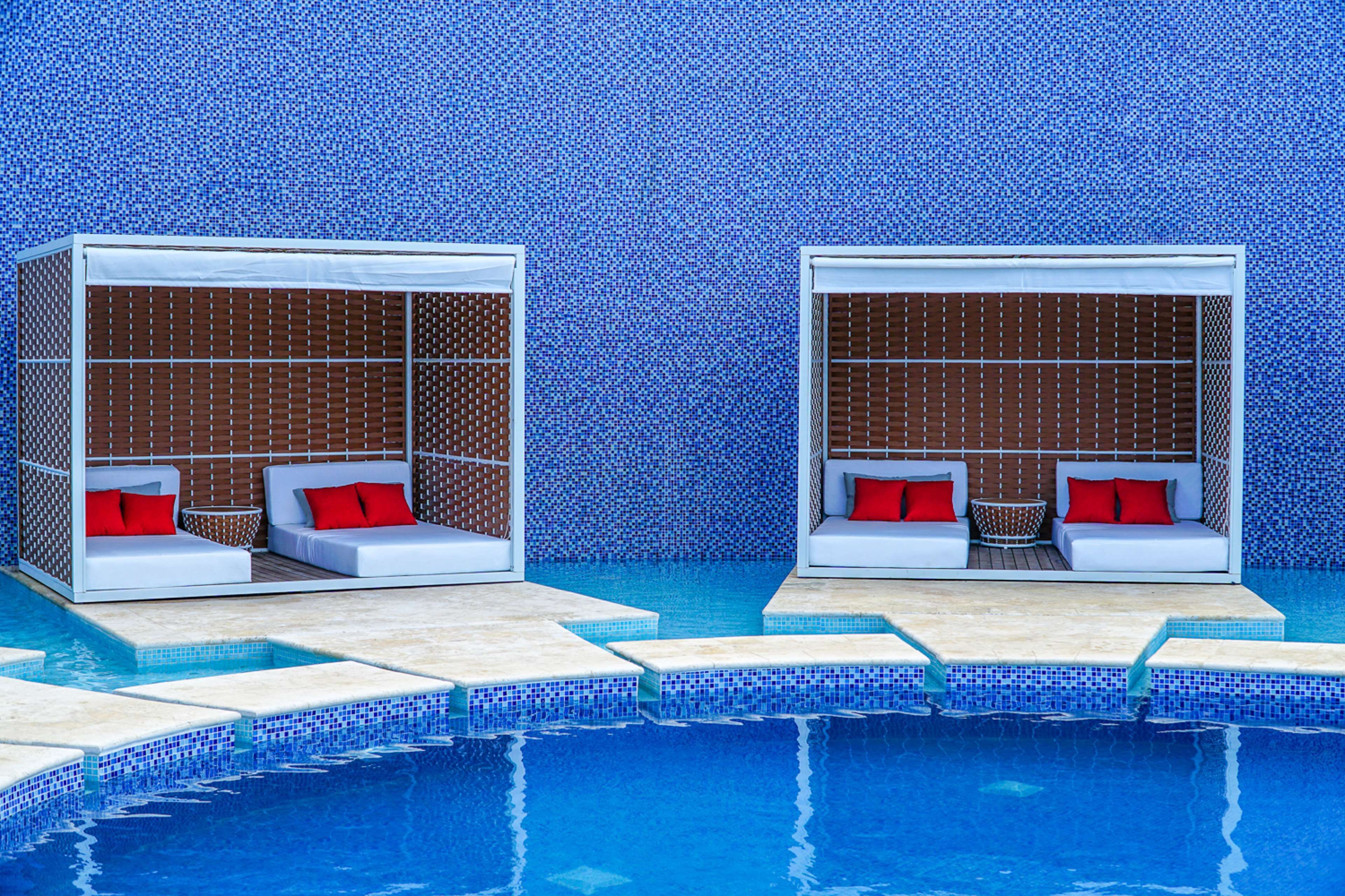 Two white, enclosed seating areas with red cushions and a small table, adjacent to a pool with blue-tiled steps.