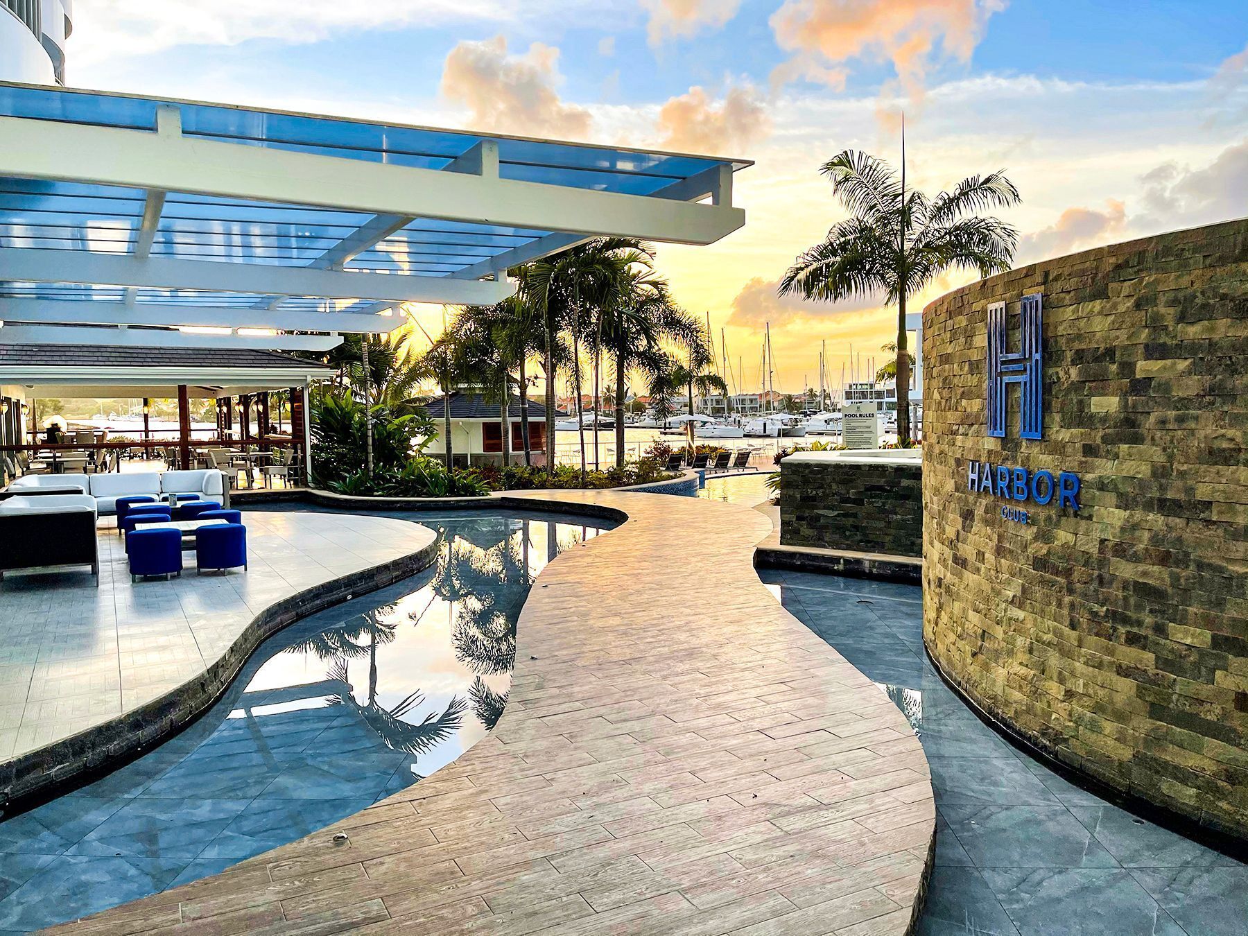 A pool area with lounge chairs, a wooden deck, and a stone wall with a sign.