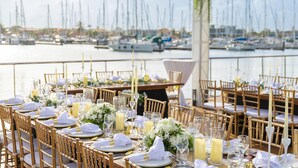 Une salle à manger avec des tables dressées pour un événement officiel, donnant sur une marina où sont amarrés des bateaux.