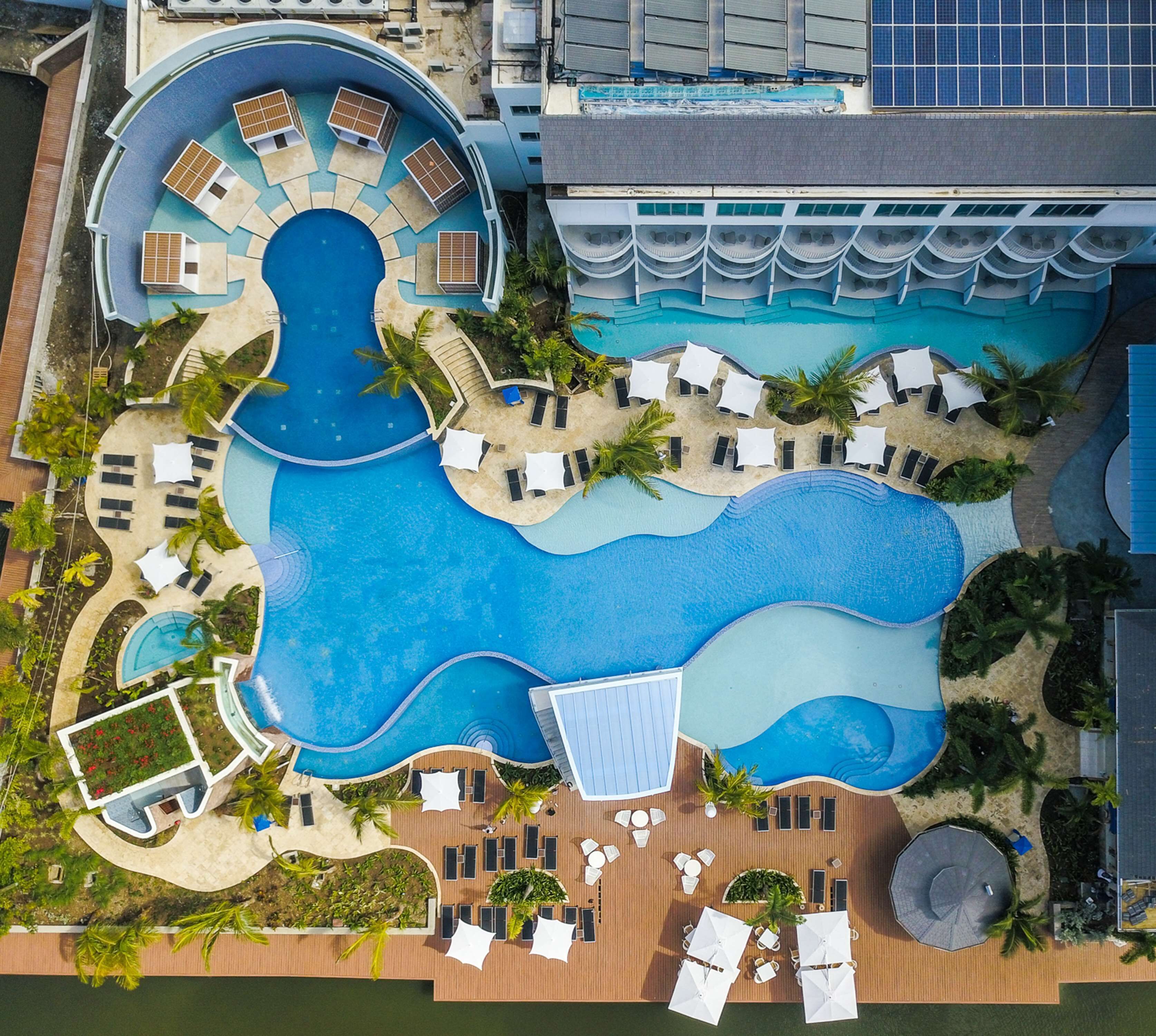 Vue aérienne d’un complexe hôtelier doté de plusieurs piscines, de chaises longues et de palmiers.