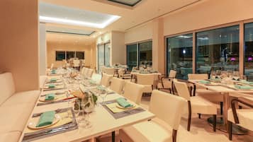 A modern dining area with long tables set for multiple guests, featuring a neutral color palette and contemporary furnishings.
