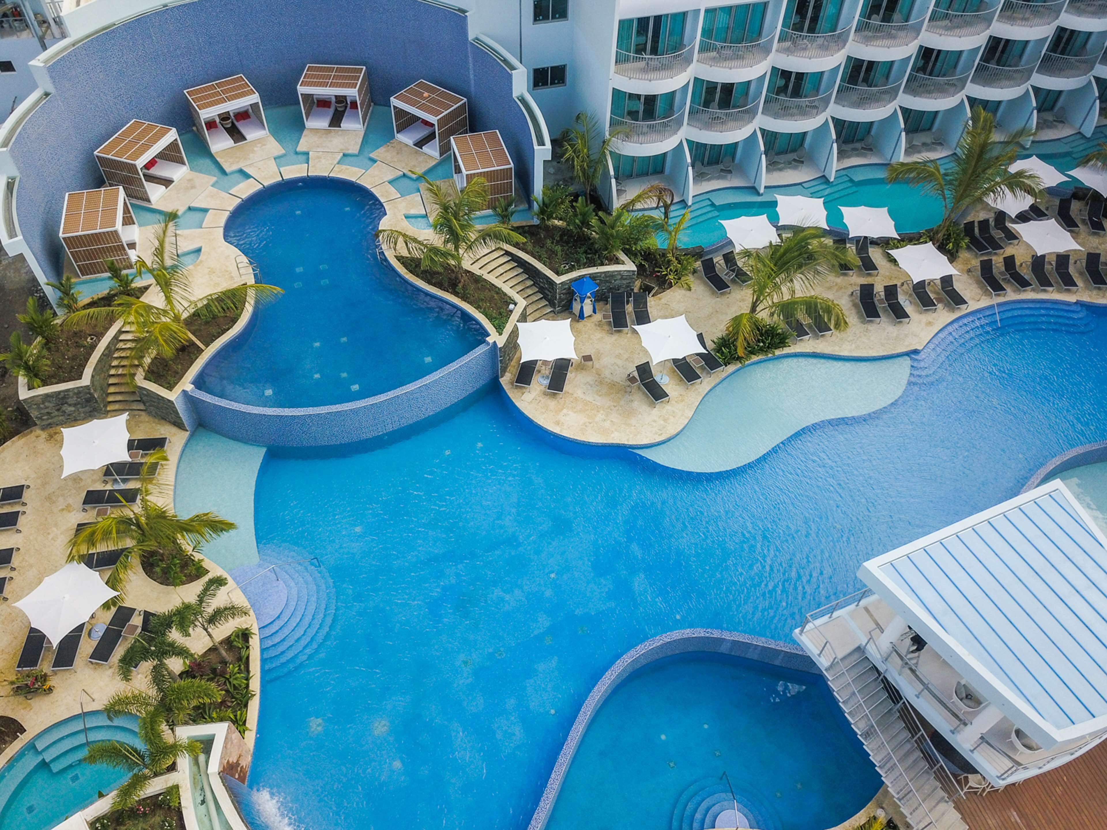 A multi-level hotel with a large, winding pool area, multiple sun loungers, and a variety of seating options.