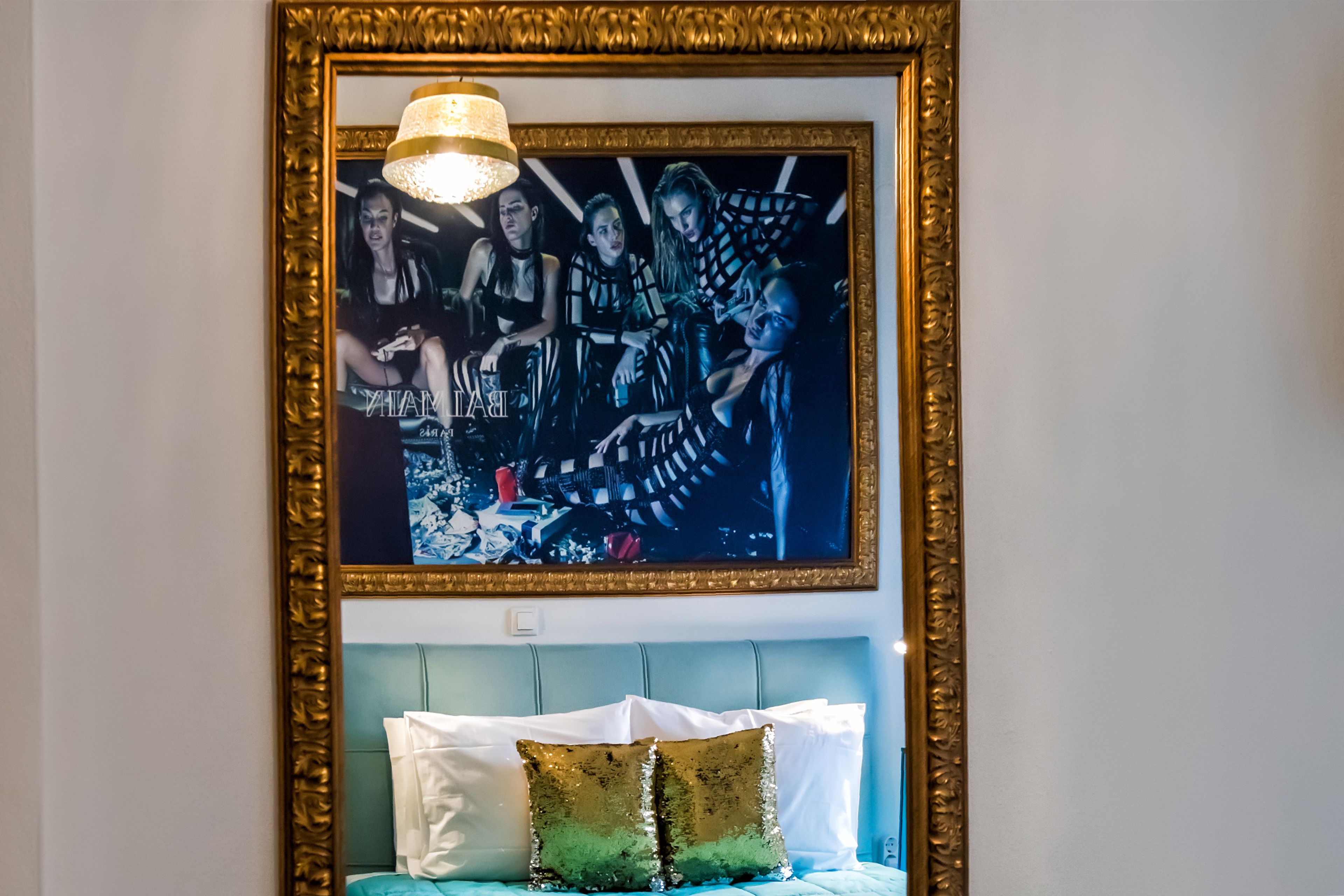 A framed artwork above a bed with a blue headboard and decorative pillows.