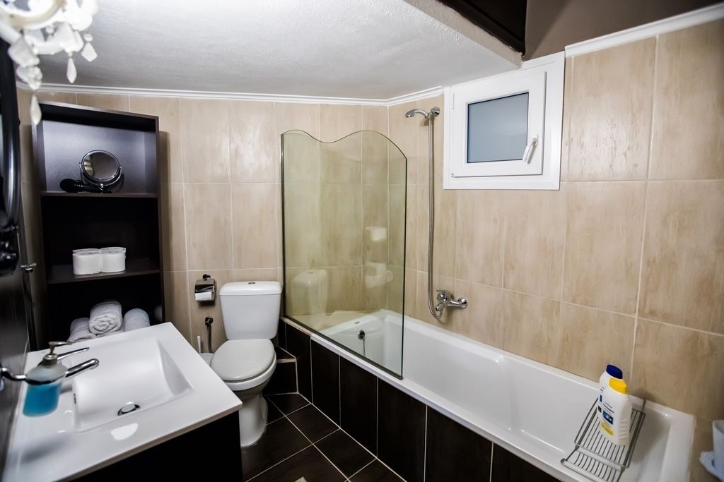 Une salle de bain avec une douche à parois de verre, un lavabo blanc, des toilettes et une étagère contenant des articles de toilette.