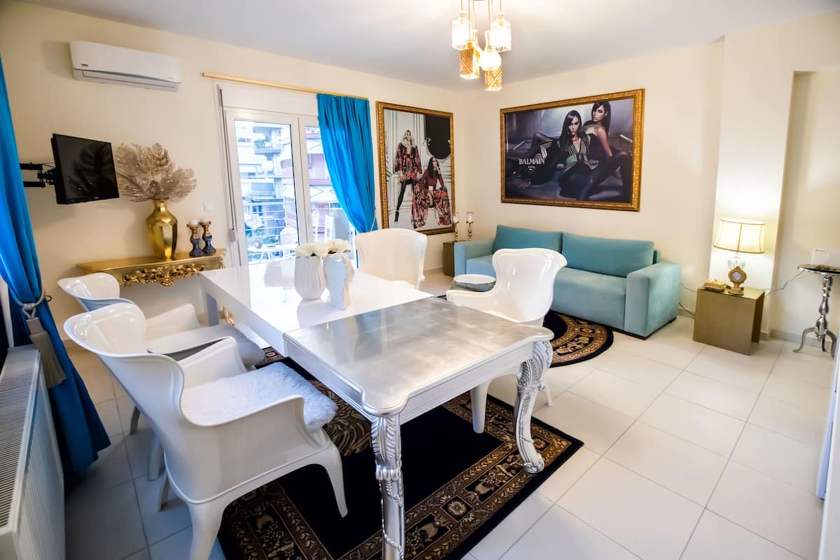 Ein modernes Wohnzimmer mit Essbereich, mit einem weißen Tisch, einem blauen Sofa und Dekorationselementen.