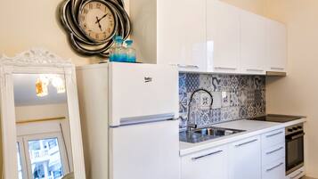 A compact kitchen with white cabinetry, a built-in sink, and a stove. A decorative clock and a mirror are mounted on the wall.