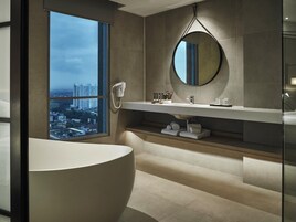 A modern bathroom with a large bathtub, a vanity with a mirror, and a view of a cityscape through a large window.