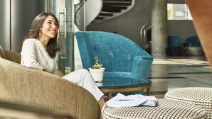 A modern interior with a curved staircase, a blue armchair, and a round table with a potted plant. - Novotel Karawang (Karawang)