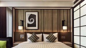 A hotel room with a large bed, two nightstands, a modern wall art piece, and a large window with blinds. - Novotel Karawang (Karawang)
