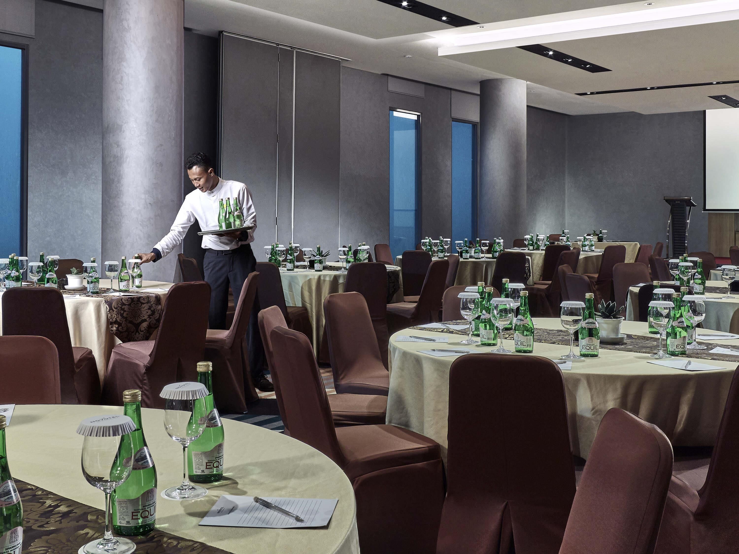 A hotel dining area with round tables, chairs, and a waiter serving.