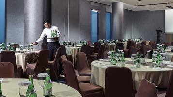 A hotel dining area with round tables, chairs, and a waiter serving.