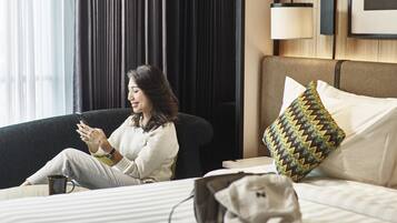 Una habitación de hotel con una cama, una silla, una lámpara y un ventanal con cortinas.