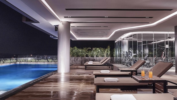 A modern indoor pool area with lounge chairs, a glass wall, and exercise equipment. - Novotel Karawang (Karawang)