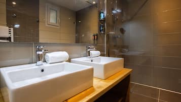 Un baño moderno con dos lavamanos blancos, un mueble de tocador de madera y una cabina de ducha de vidrio.