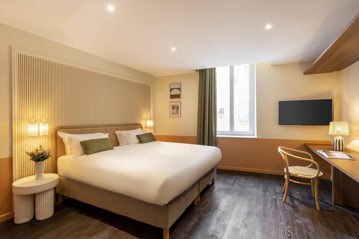 Ein Hotelzimmer mit einem großen Bett, einem Schreibtisch mit Stuhl, einem Fernseher und einem Fenster mit Vorhängen.