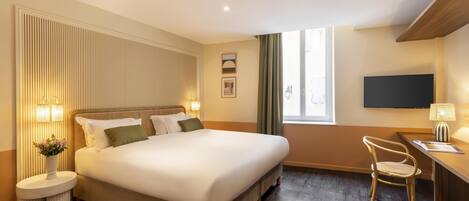 Ein Hotelzimmer mit einem großen Bett, einem Schreibtisch mit Stuhl, einem Fernseher und einem Fenster mit Vorhängen.