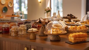 A buffet with various food items, including pastries, breads, and desserts, displayed on wooden stands and under glass domes. - Grand Hôtel d’Orange, BW Signature Collection (Orange)