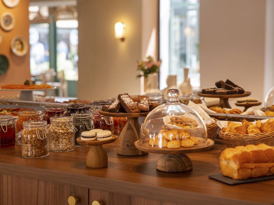 A buffet with various food items, including pastries, breads, and desserts, displayed on wooden stands and under glass domes.