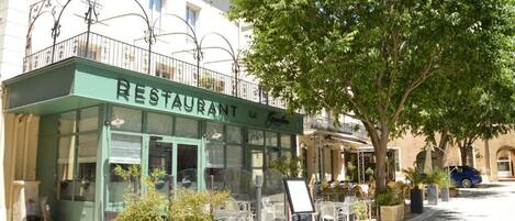 A restaurant with outdoor seating, a green awning, and a tree in front.