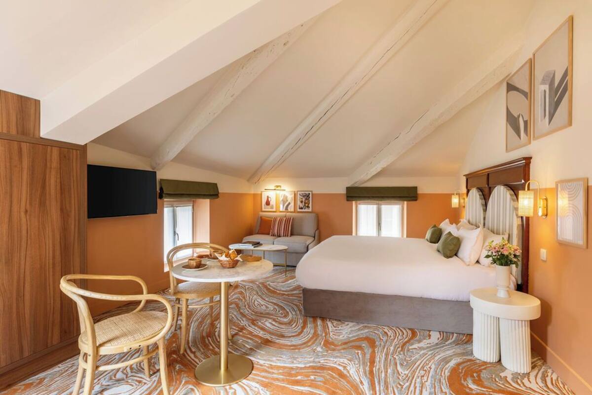 Ein Schlafzimmer mit einem großen Bett, einem kleinen Tisch, zwei Stühlen und einem Fernseher an der Wand.