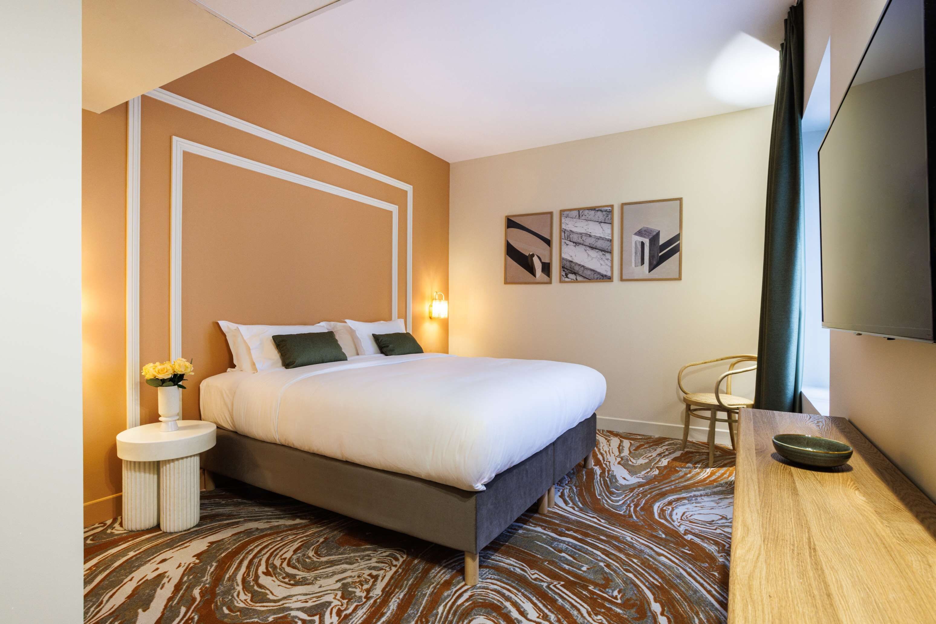 A hotel room with a bed, bedside tables, a TV, and artwork on the wall.