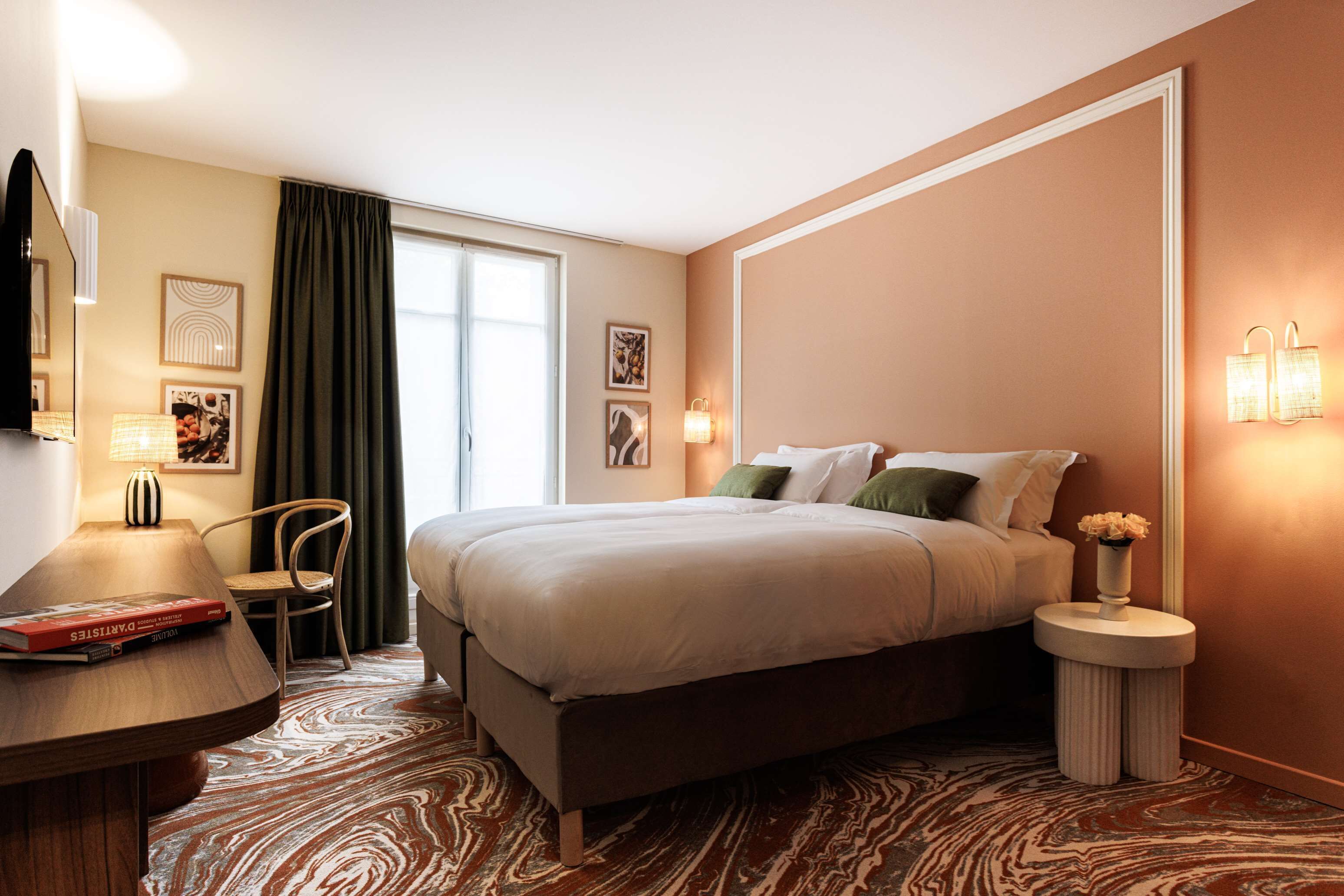 A hotel room with a large bed, a desk with a lamp, a chair, and a small side table with a vase.