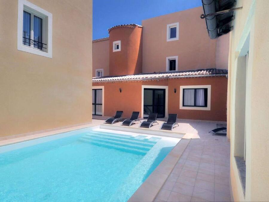 A swimming pool with lounge chairs, a building with a tiled roof, and a clear sky.