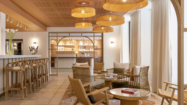A modern lobby with wicker furniture, a reception desk, and a view of the kitchen area. - Grand Hôtel d’Orange, BW Signature Collection (Orange)