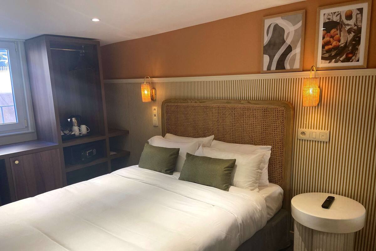Ein ordentlich bezogenes Bett mit Kissen, ein Nachttisch mit Fernbedienung und Wandleuchten.
