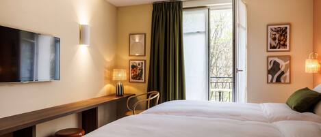 A hotel room with a bed, a desk, a chair, a TV, and a window with curtains.