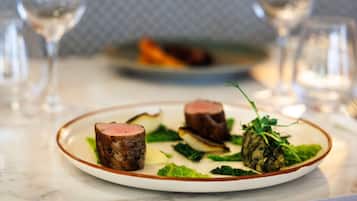 A plate of food with two pieces of meat and greens on a white plate with a brown rim.