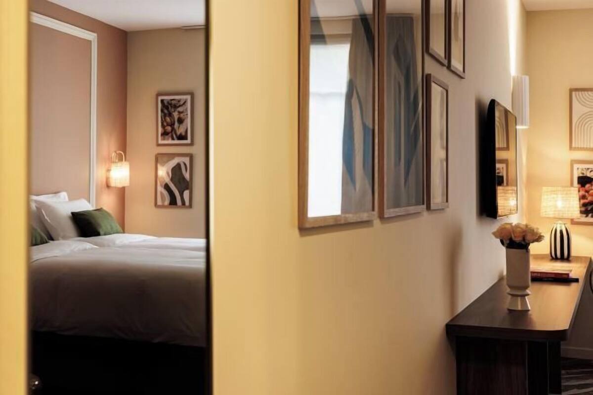 Ein Hotelzimmer mit einem Bett, einem Schreibtisch, einer Lampe und gerahmten Kunstwerken an der Wand.