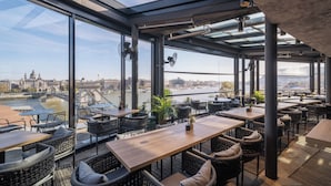 Ein modernes Restaurant mit großen Fenstern und Blick auf einen Fluss sowie die Stadtlandschaft.