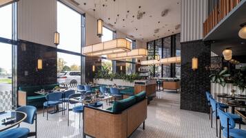 A modern restaurant interior with hexagonal tiled flooring, blue upholstered chairs, and a central seating area with a woven bench.