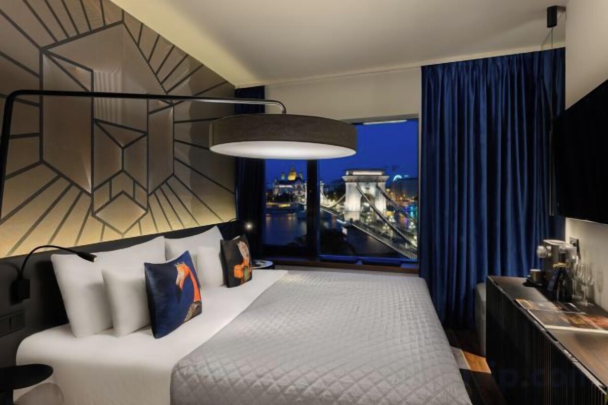 Habitación de hotel con una cama grande, un escritorio, vistas a la ciudad y un diseño moderno de pared geométrica.