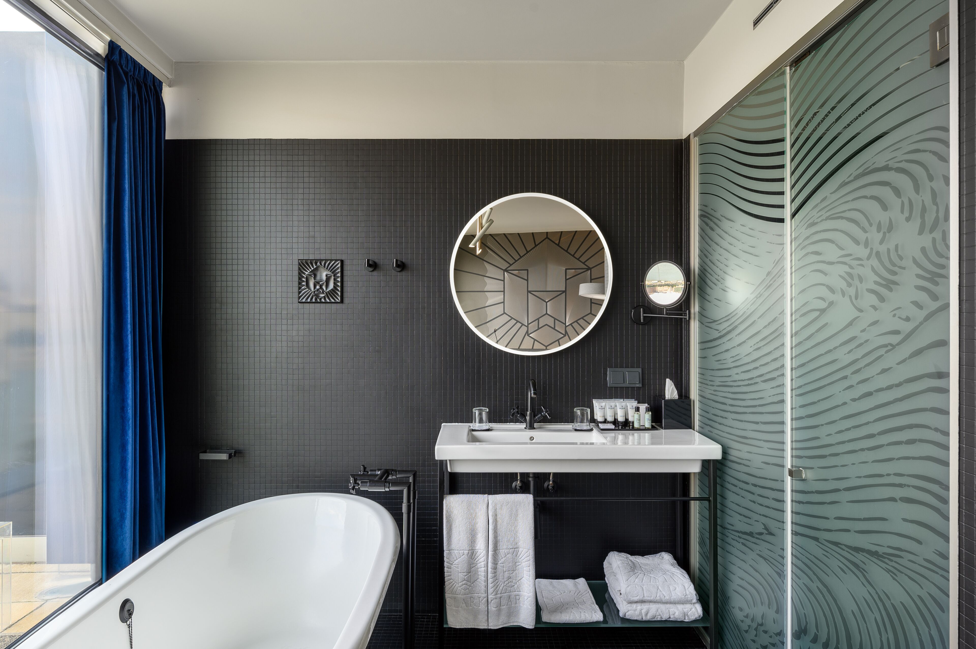 A modern bathroom with a freestanding bathtub, a round mirror, and a glass shower enclosure.