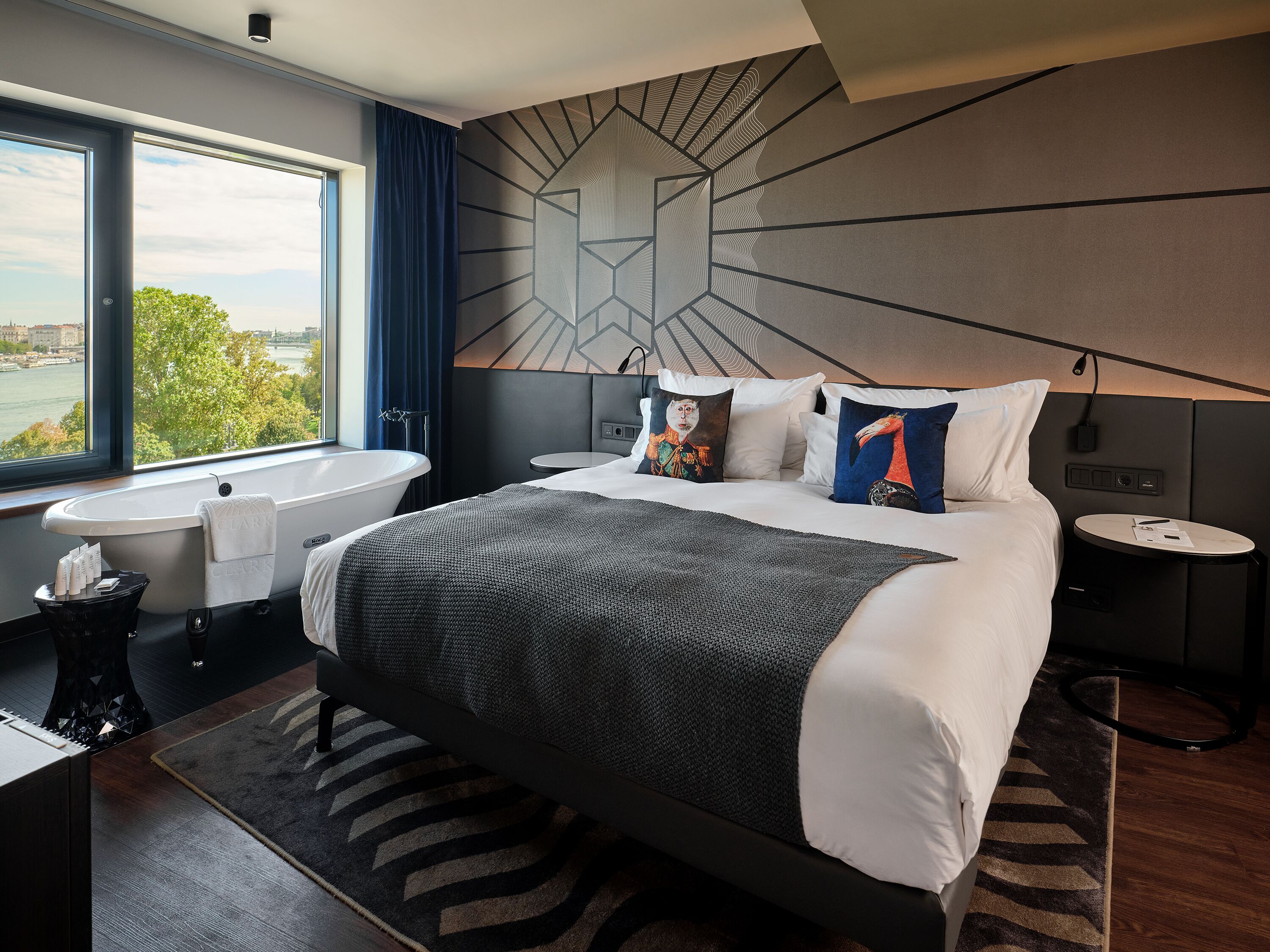 Un hotel moderno con una cama grande, vistas a la ciudad, una bañera y una mesa redonda.